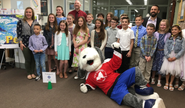 Group of children and adults posing with a large mascot in a red shirt at a school event