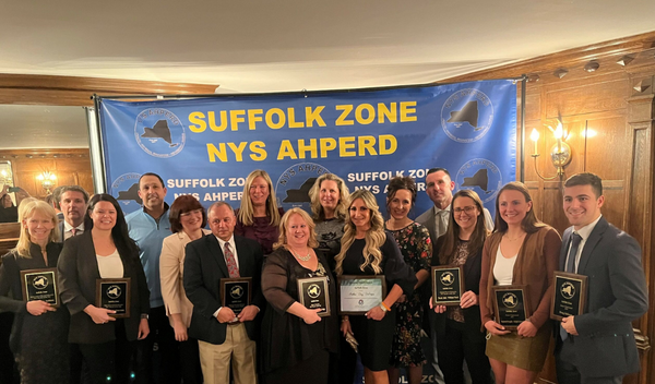 Group of people holding plaques at an awards ceremony beneath a blue “SUFFOLK ZONE NYS AHPERD” banner.
