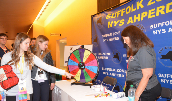 People at a Suffolk Zone NYS AHPR booth with a colorful prize wheel at an indoor event
