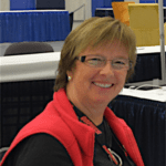 Smiling woman with glasses in a red vest at a booth with blue table skirting