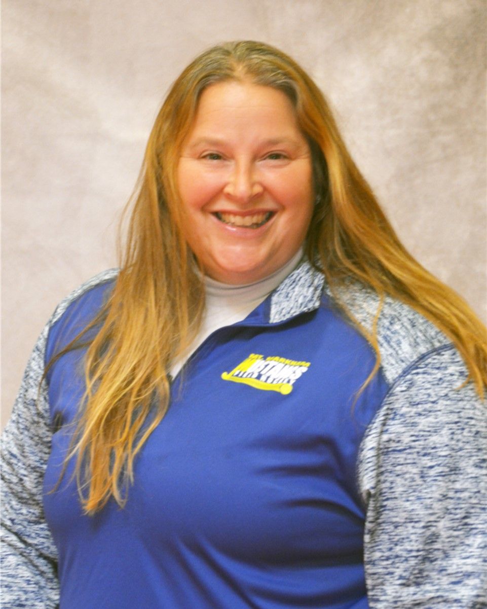 Smiling person in blue collared shirt with logo, against a neutral studio backdrop