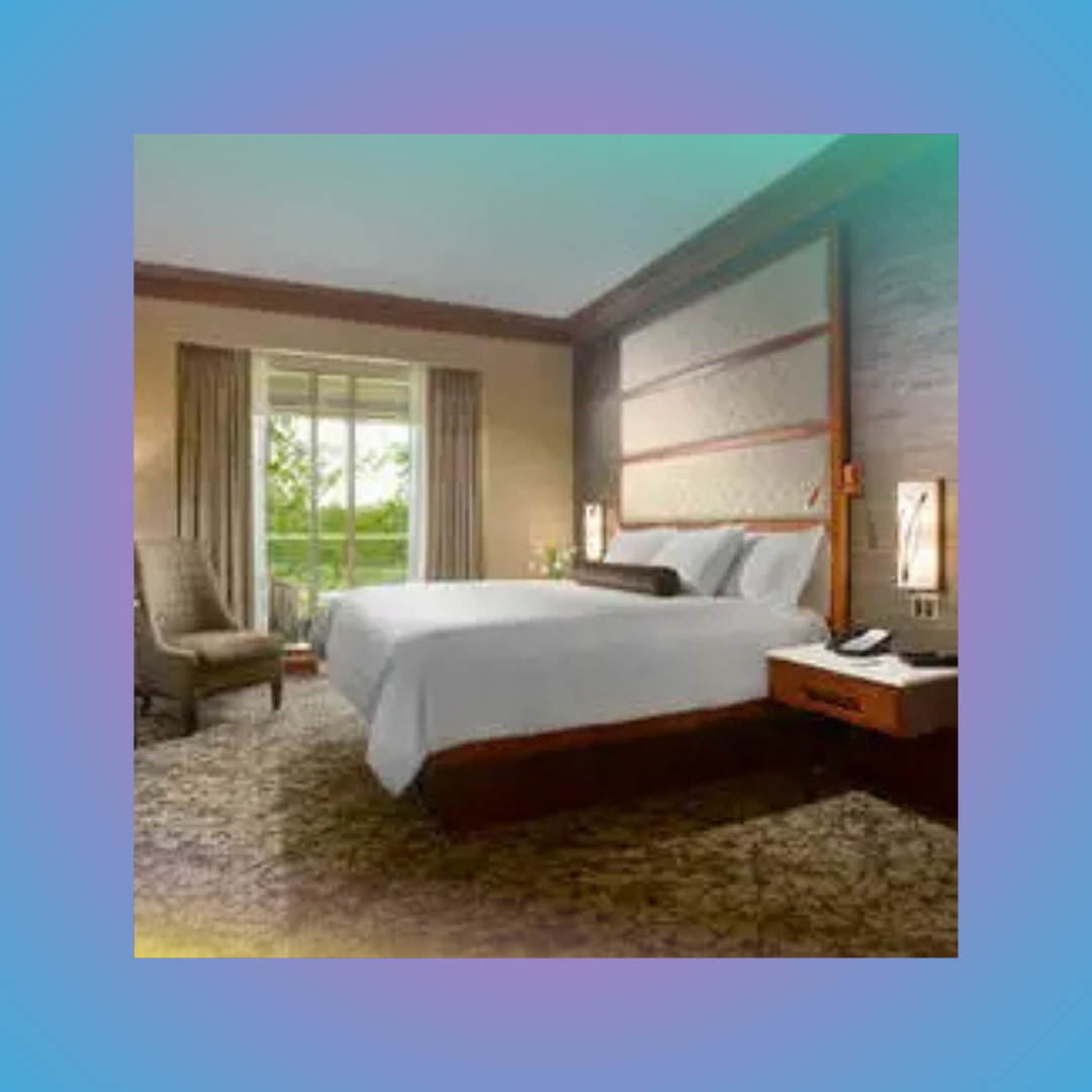 Modern hotel room with a king bed, armchair, bedside table, and balcony doors overlooking greenery