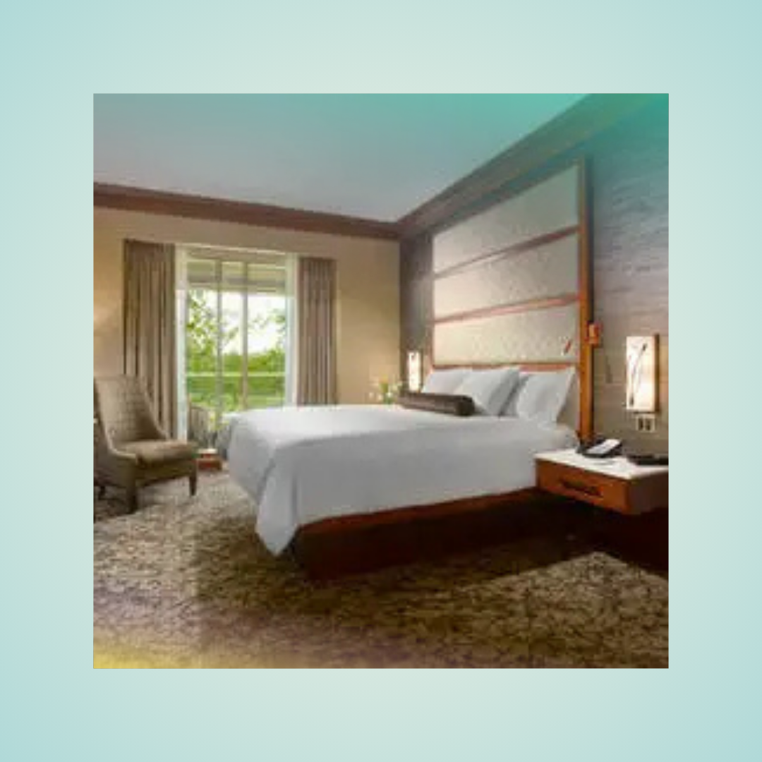 Modern hotel room with a king bed, armchair, bedside table, and balcony doors overlooking greenery