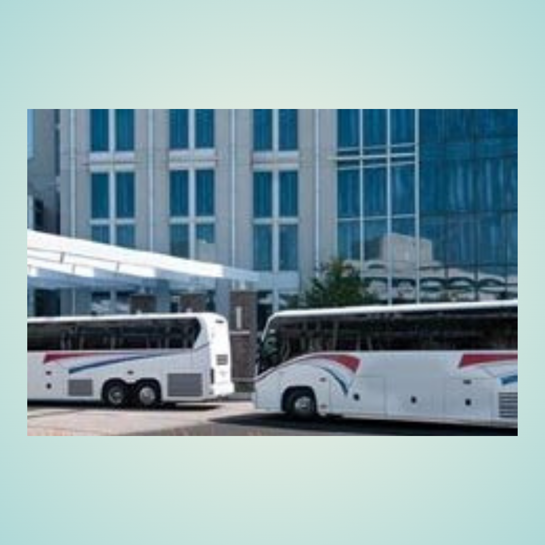Two white tour buses parked outside a modern glass building
