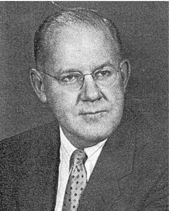 Black-and-white portrait of a man in a suit, tie, and glasses, facing slightly to the side.