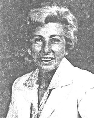 Black-and-white portrait of a smiling woman in a light jacket, facing the camera.