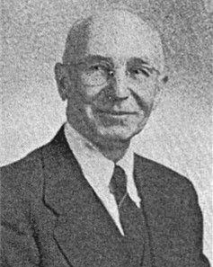 Portrait of a smiling man in a dark suit and tie against a plain background