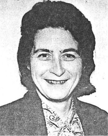 Black-and-white portrait of a smiling person in a blazer and patterned blouse.
