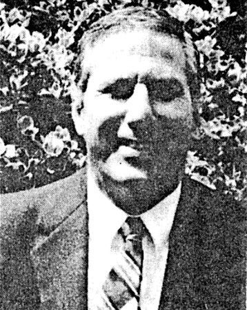 Black-and-white portrait of a smiling man in a suit and striped tie outdoors