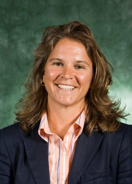 Smiling person in a navy blazer and striped shirt against a green studio background