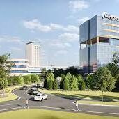 Modern office campus with glass towers, trees, and a curved road with cars and pedestrians.