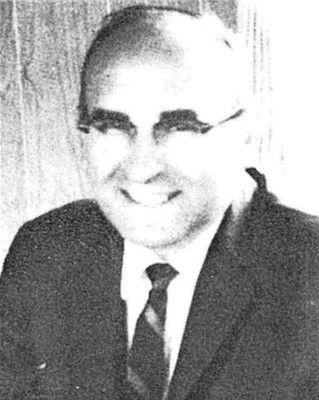 Black-and-white portrait of a smiling man in a suit and tie against a plain background.
