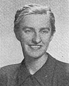 Black-and-white portrait of a smiling person in a dark collared jacket.