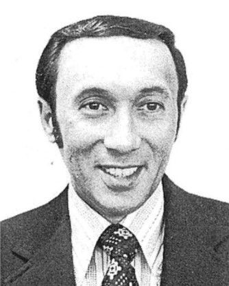 Black-and-white portrait of a smiling man in a suit, shirt, and patterned tie.