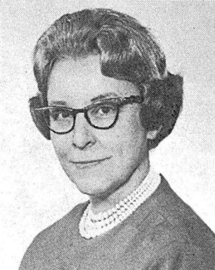 Black-and-white portrait of a person wearing glasses, a pearl necklace, and a sweater, looking at the camera.