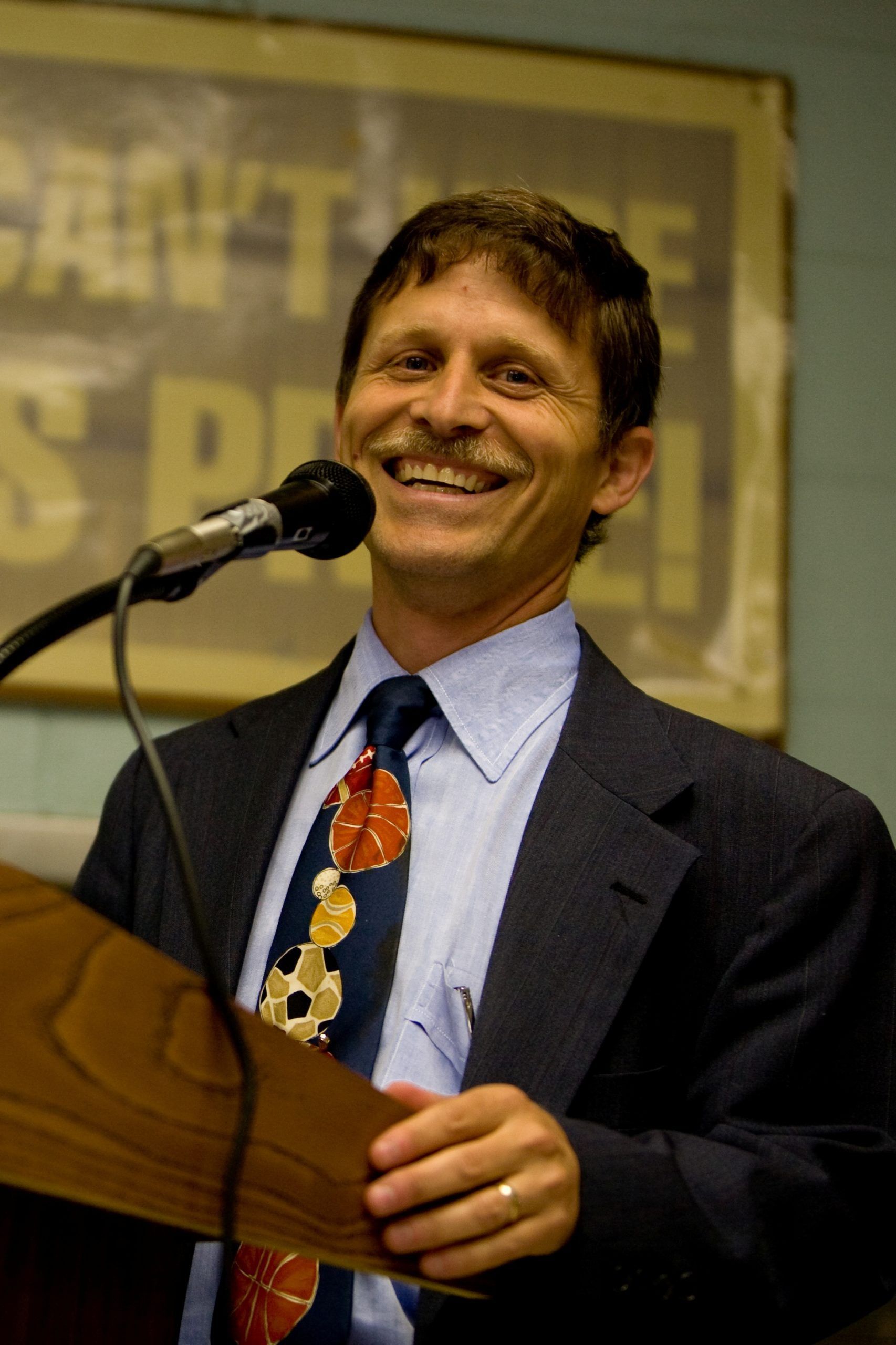 Smiling man in a suit speaking at a podium with a microphone.