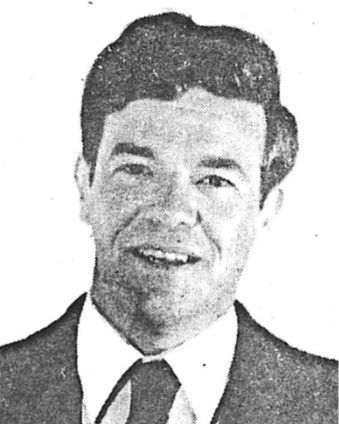 Black-and-white headshot of a smiling man in a suit and tie
