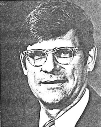 Black-and-white portrait of a man wearing glasses and a suit, facing the camera with a neutral expression