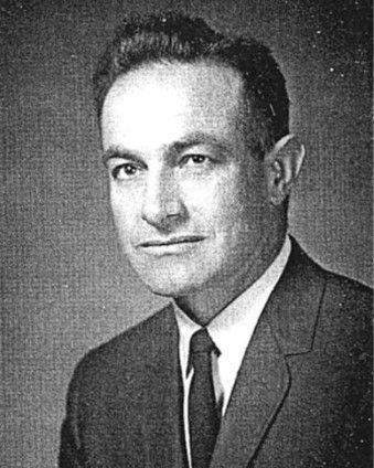 Black-and-white portrait of a man in a suit and tie, facing slightly left with a neutral expression