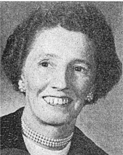 Black-and-white portrait of a smiling woman with short dark hair, pearl necklace, and earrings.