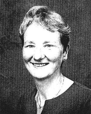 Black-and-white portrait of a smiling person with short hair against a dark background