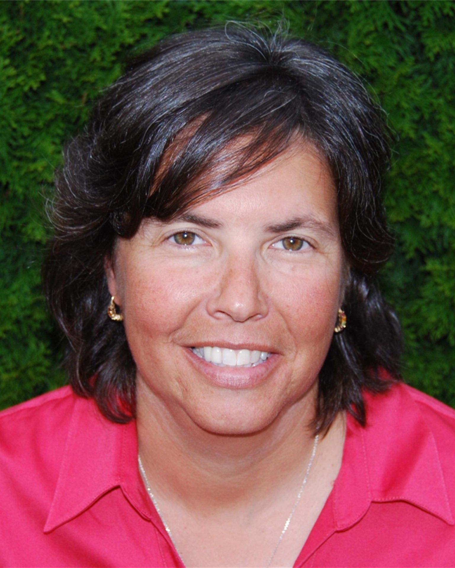 Smiling woman in a pink shirt against a green leafy background