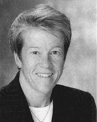 Portrait of a smiling person in a dark blazer against a gray studio background