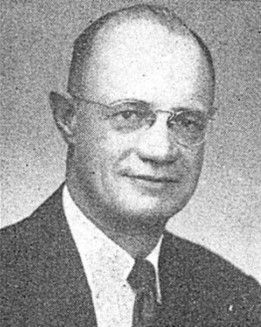 Black-and-white portrait of a man in a suit, tie, and glasses, facing slightly left.