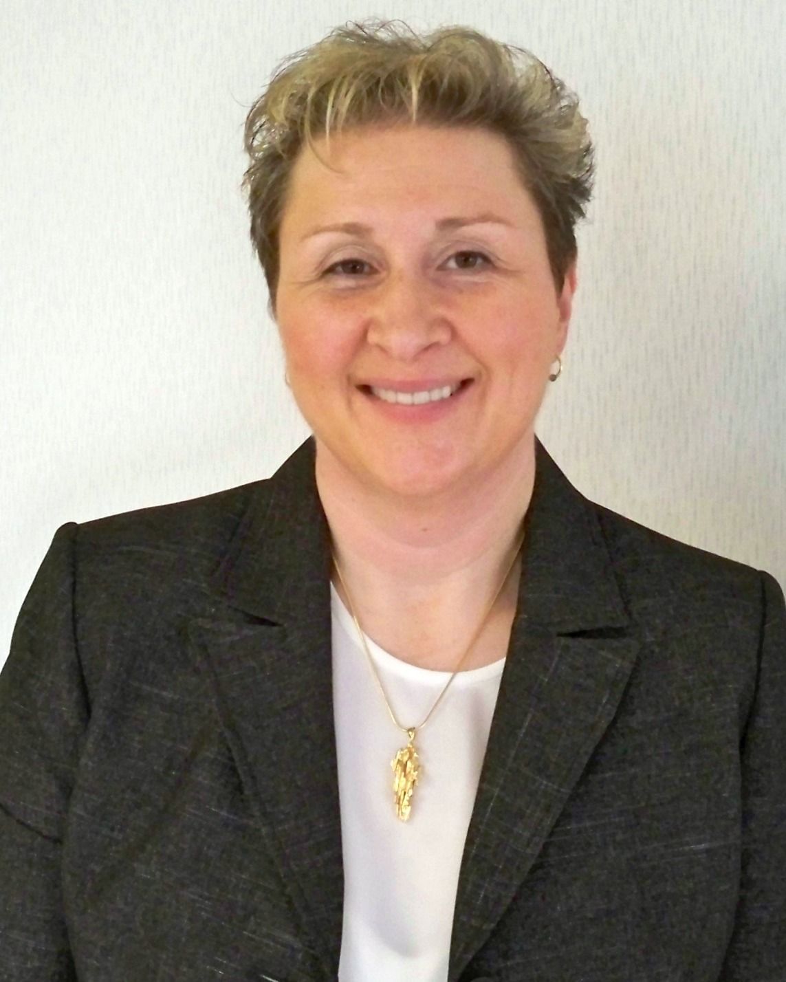 Portrait of a smiling person in a dark blazer and white top against a light background