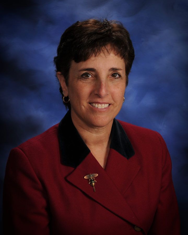Studio portrait of a person in a maroon blazer against a blue background, smiling gently
