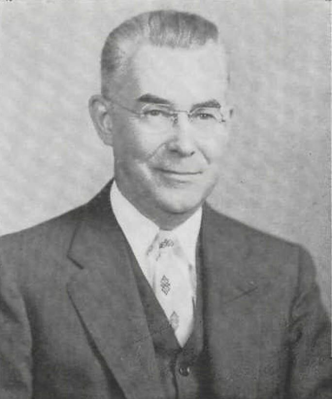 Black-and-white portrait of a man in a suit and tie, facing forward with a slight smile.