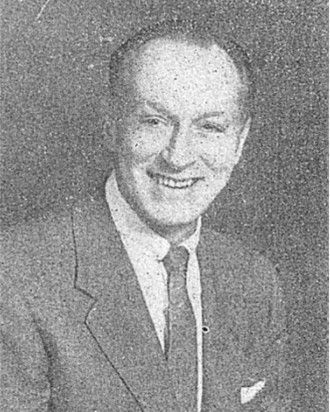 Grainy black-and-white portrait of a smiling man in a suit and tie.