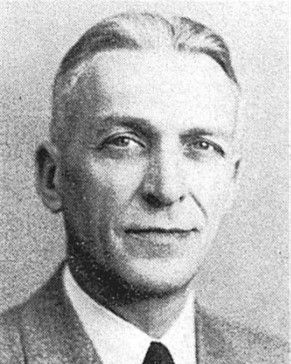 Black-and-white portrait of a man in a suit, looking at the camera with a slight smile.