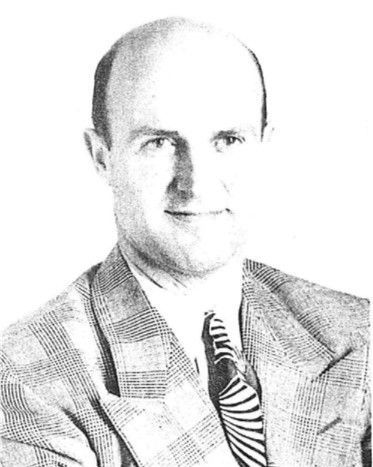 Black-and-white portrait of a man in a plaid suit jacket and striped tie, facing the camera.