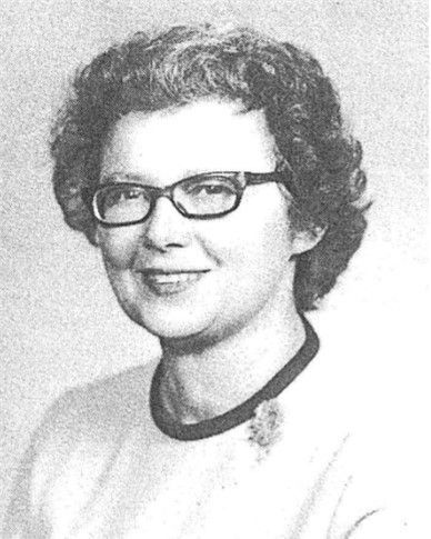 Black-and-white portrait of a smiling person wearing glasses and a dark-collared top