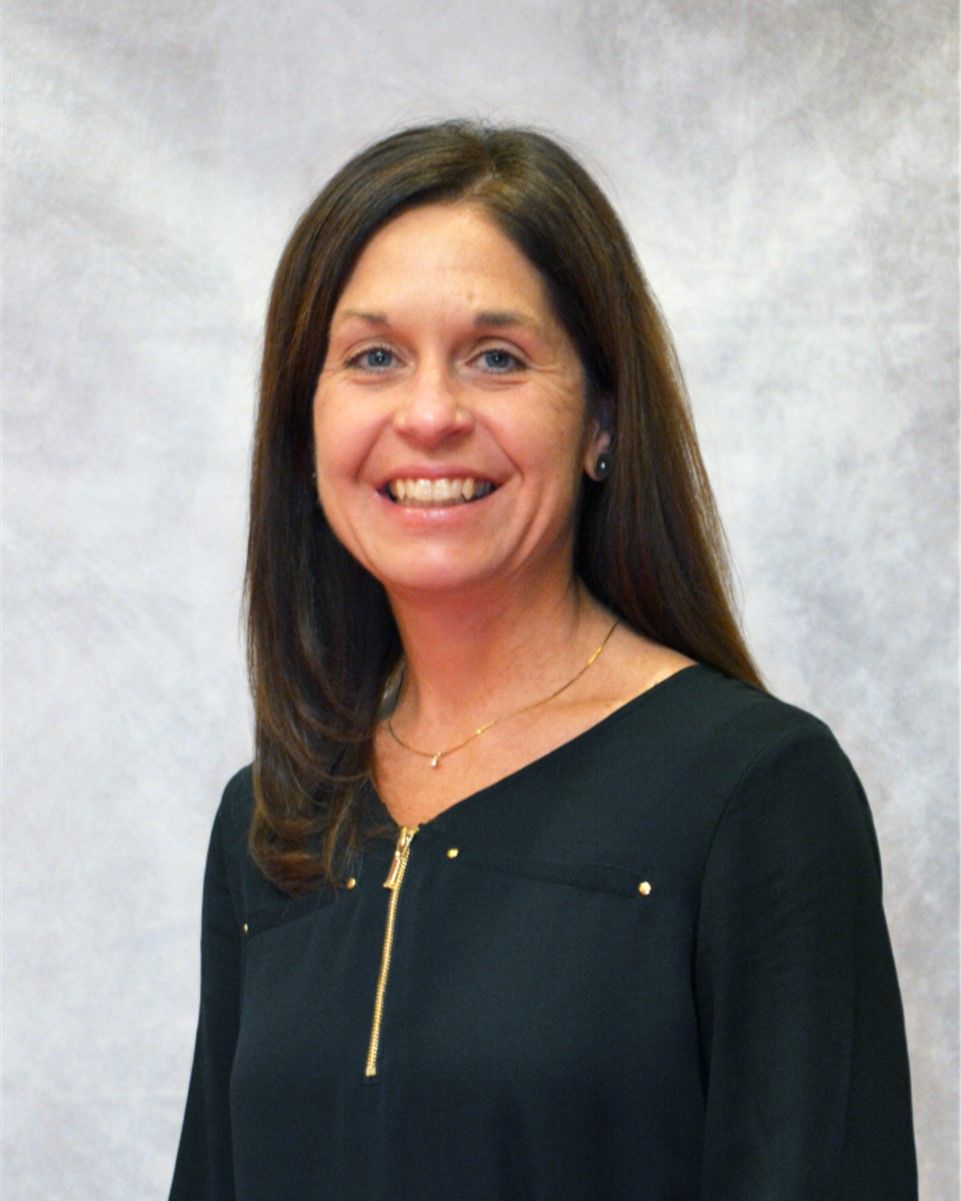 Woman smiling in a black top against a gray studio backdrop.