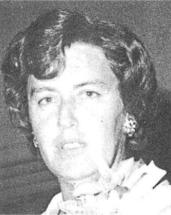 Black-and-white portrait of a person with wavy hair and a light floral collar, facing the camera.