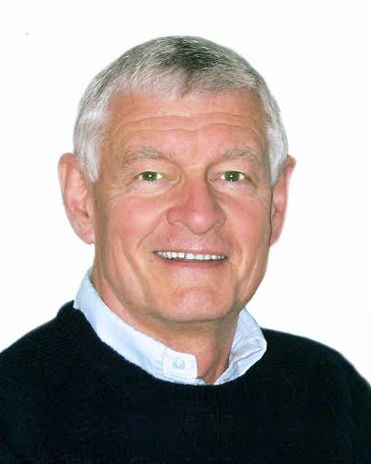 Portrait of a smiling man with short gray hair, wearing a black sweater over a light blue collared shirt.