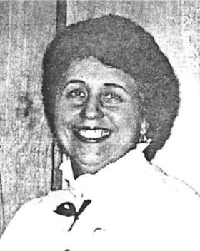 Black-and-white portrait of a smiling person with short curly hair in a white blouse.
