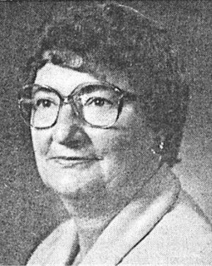 Black-and-white portrait of a woman wearing glasses, looking slightly to the side and smiling faintly