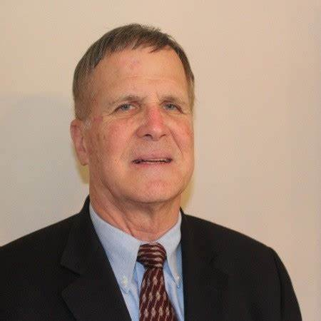 Portrait of a man in a dark suit and patterned tie against a plain beige background