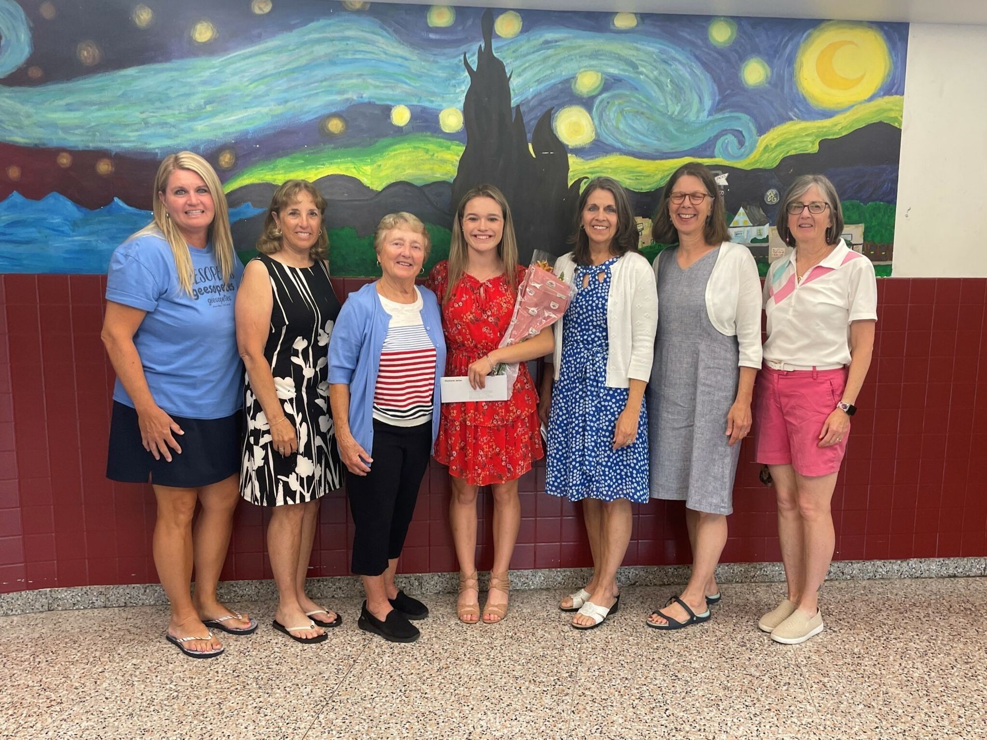 Seven people stand smiling in front of a colorful starry mural with a black cat silhouette.
