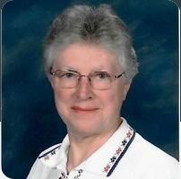 Portrait of an older woman with glasses, short gray hair, and a white blouse against a blue background