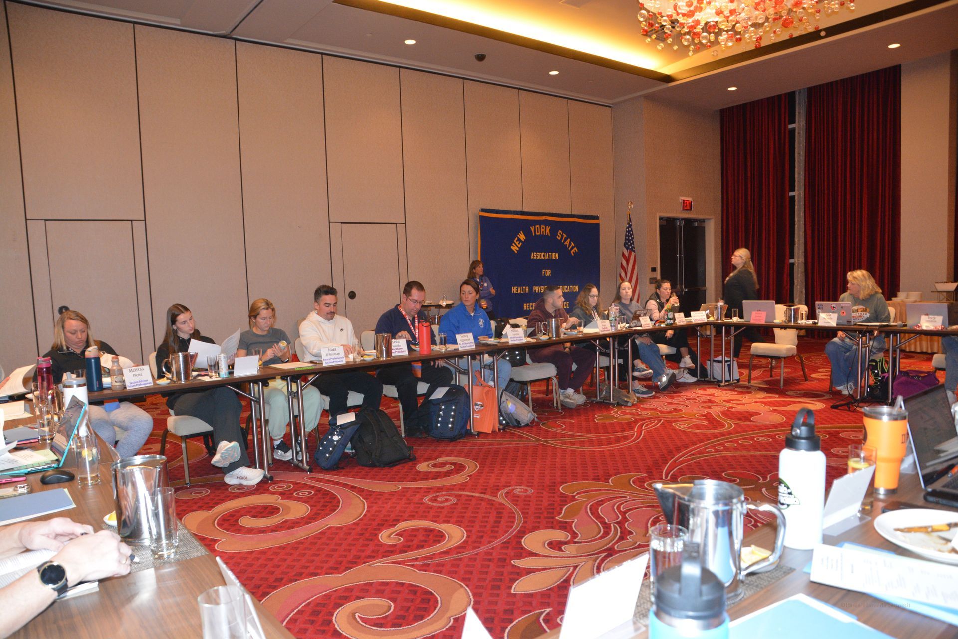 Conference meeting room with people seated around tables, discussing under warm lighting