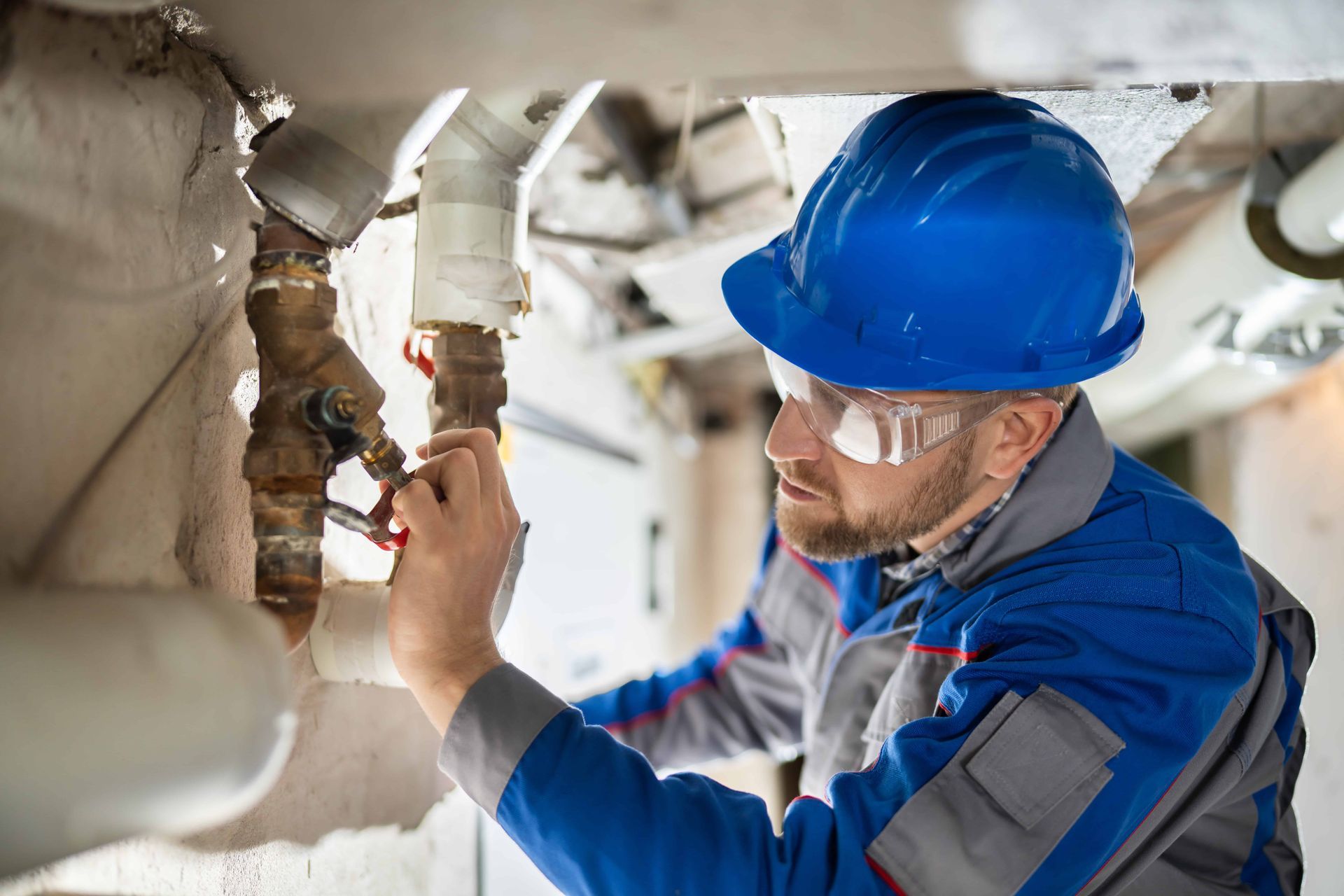 Plumber in blue uniform and hard hat repairing pipes with a wrench, focused, in a mechanical room.