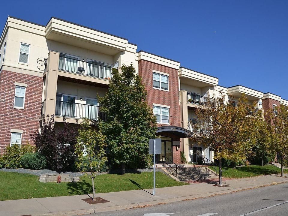 Apartment building with balconies, brick and beige exterior, and a front lawn under a clear blue sky