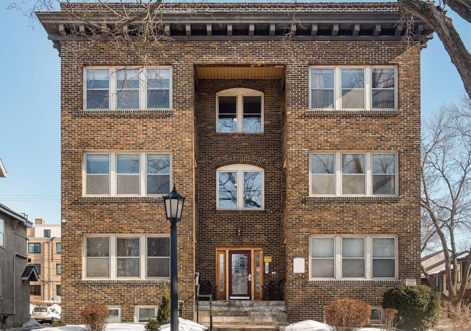 Brick apartment building facade with symmetrical windows and a central entrance, viewed from the street