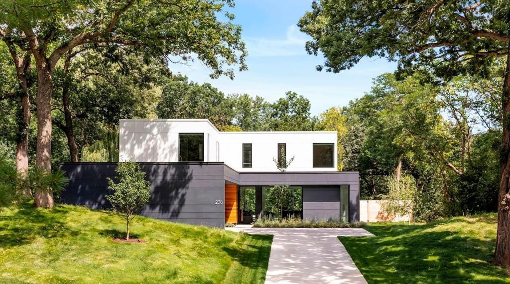 Modern white house with dark accents, framed by trees and a green lawn, with a path leading to the entrance