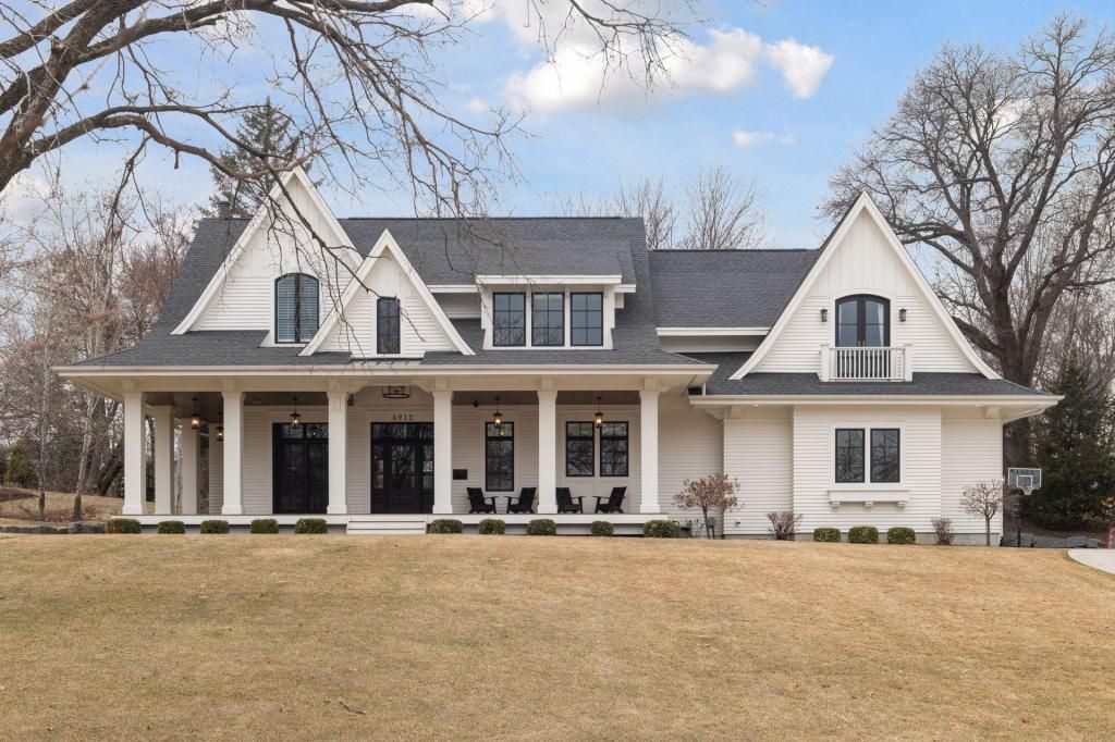 Large white house with gray roof and front porch on a grassy lot in a rural setting
