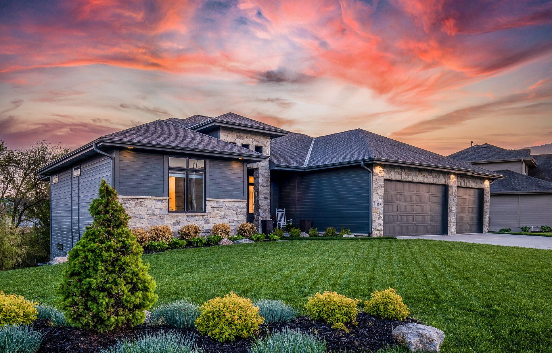 Modern suburban house with stone facade, three-car garage, and colorful sunset sky
